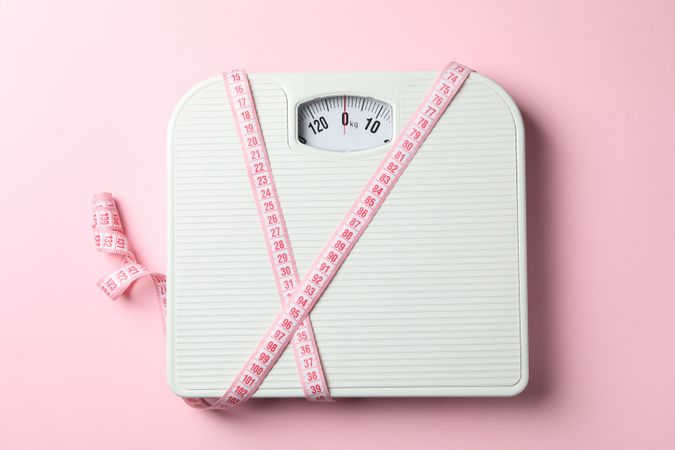 Scales and measuring tape on pink background. Weight loss concept