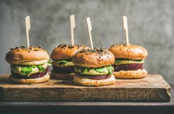 Upright fresh vegan burgers on seeded buns with skewer on wooden board