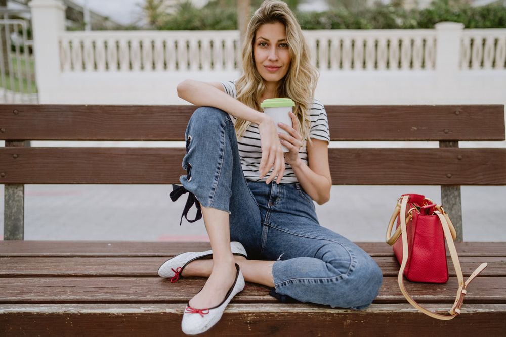 Relaxed woman with disposable cup of coffee sitting on street bench