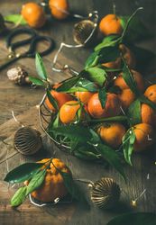Freshly picked tangerines in wire bowl, with leaves on wooden table, with Christmas decorations