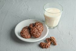 Glass of milk and plate with chocolate cookies on grey table, space for text
