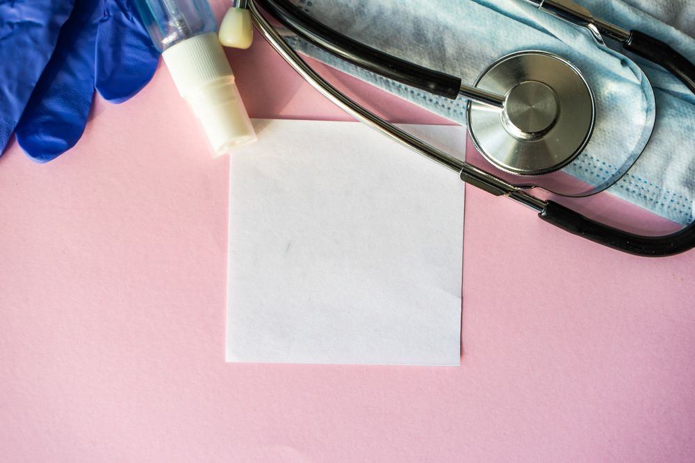 Top view of pink table with stethoscope, facemask, protective gloves and spray