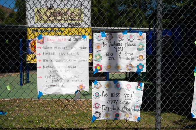 Three homemade signs from teachers to their students taped to chainlink fence at school