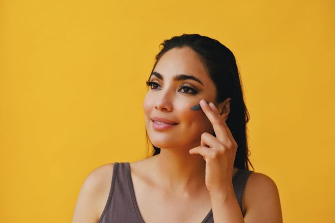 Happy Latina woman applying clay mask with hand, copy space