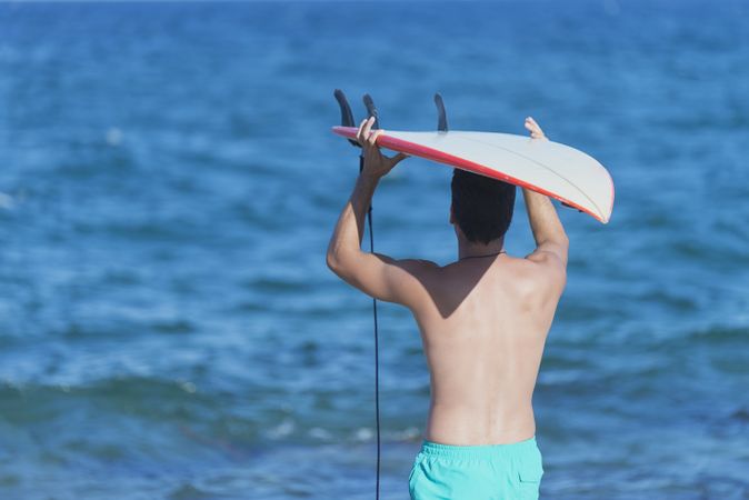 Mid body shot of male surfer looking out to the ocean with board on head, copy space