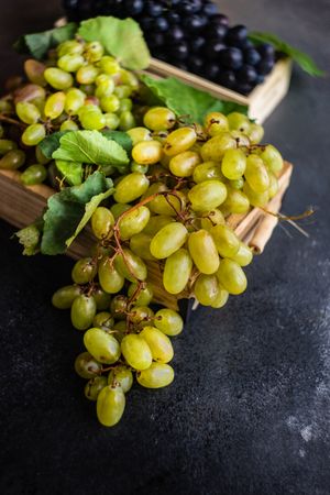 Box of delicious fresh green grapes with leaves on counter