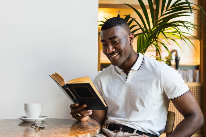 Smiling Black man reading book with drink in cafe