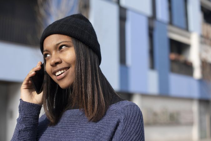 Female in wool hat and blue sweater chatting on phone on sunny day with space for text