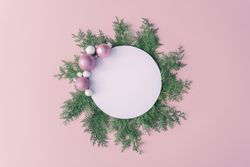 Christmas frame made of winter plants and pink baubles on pink table background