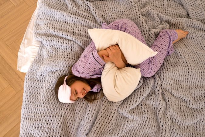 Teenage girl cuddling a pillow, wearing a sleep mask