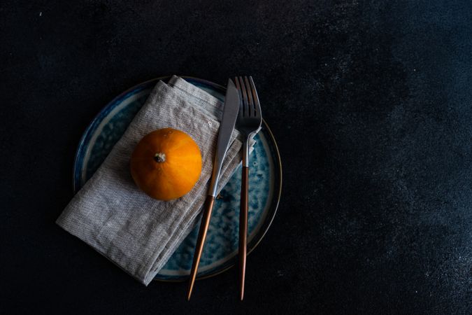 Top view of elegant cutlery with single orange squash on blue tableware