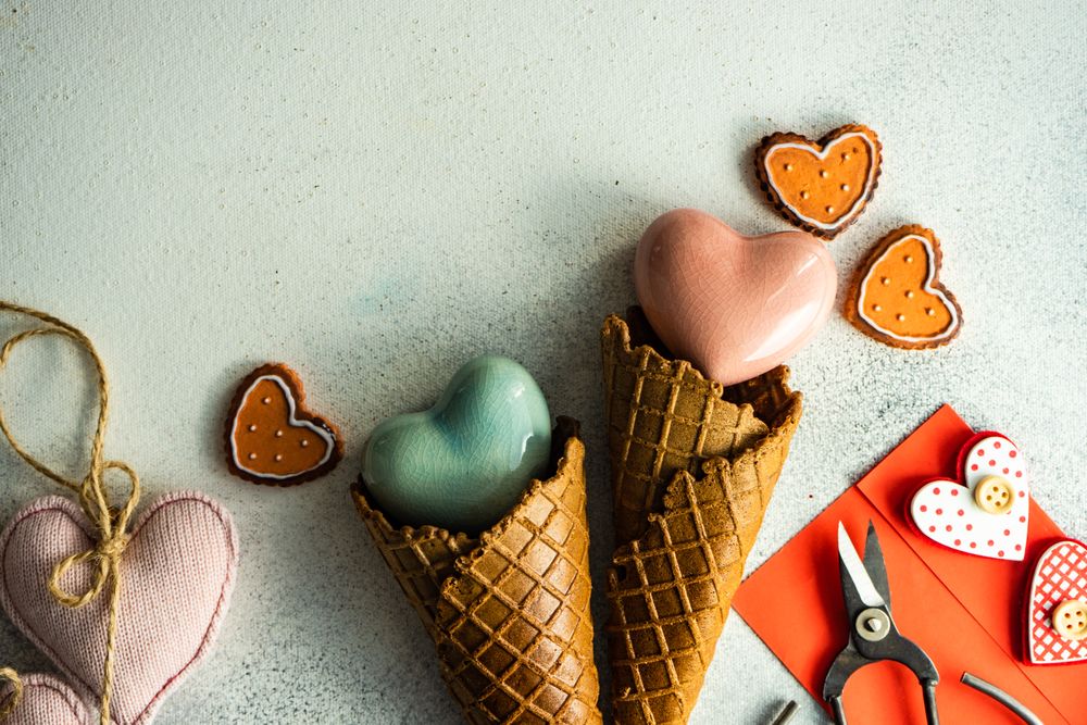 Red heart ornaments in waffle cone with envelope and gift on grey background