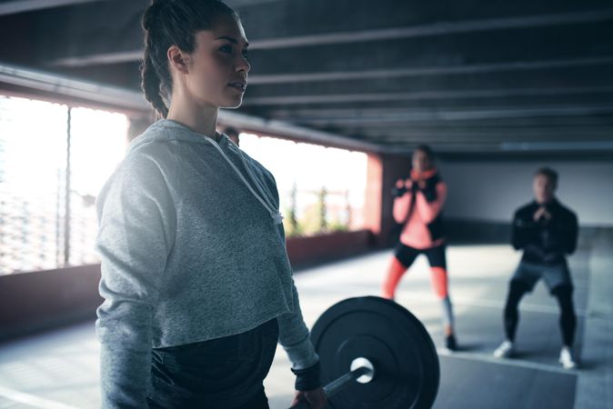 Woman in athletic gear deadlifting with a heavy barbell with people in the background