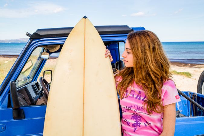 Woman with surfboard near car at seaside