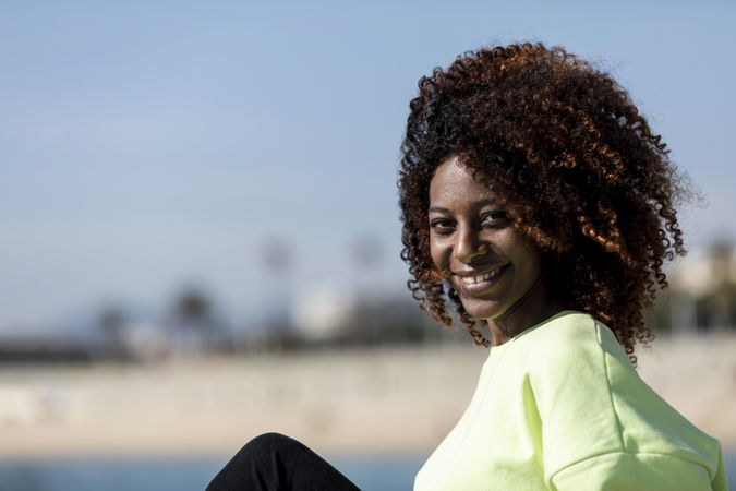 Confident female sitting near shoreline in bright green shirt