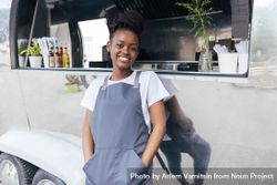 Happy Black woman in apron standing proudly outside her food truck 0Lmkr5