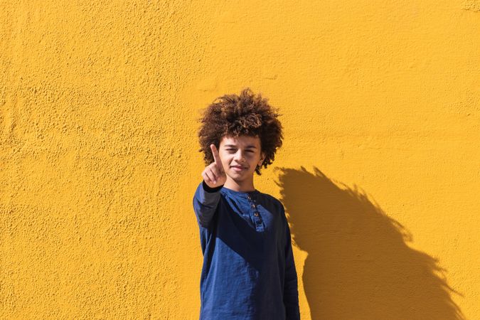 Black boy with curly hair pointing at camera