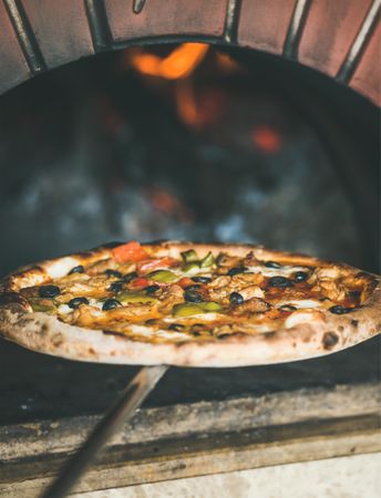 Pizza coming out of wood fire pizza oven