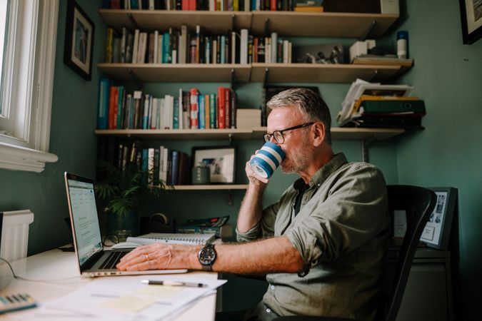 Mature man working in comfortable home office sipping coffee