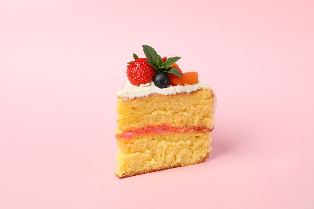 Piece of berry cream cake on pink background. Delicious dessert