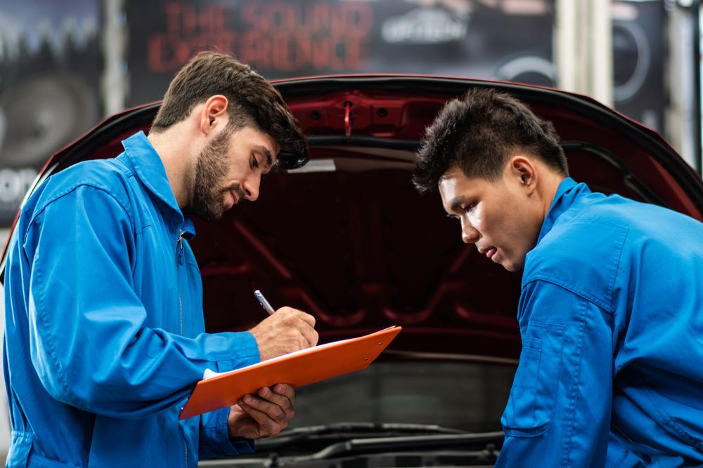 Two male auto workers standing working on engine