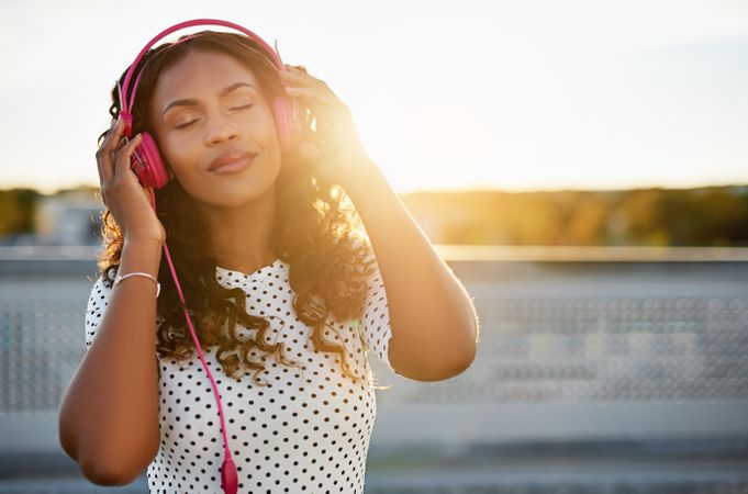 Attractive Black woman holding headphones to her ears outside