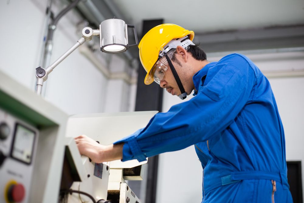 Side view of Asian male in blue jumpsuit and yellow hard hat working with machinery