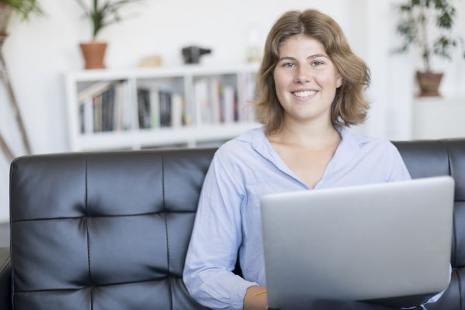 Happy woman sitting on a sofa at home working on a laptop