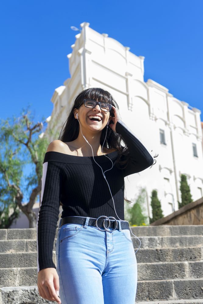 Young happy woman wearing earphones spending free time outdoors in the sun
