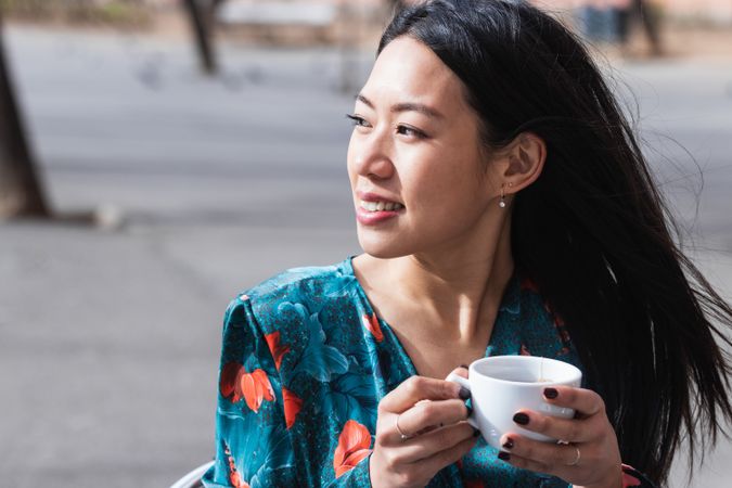 Long-haired brunette Asian woman having a coffee on a terrace of a cafe