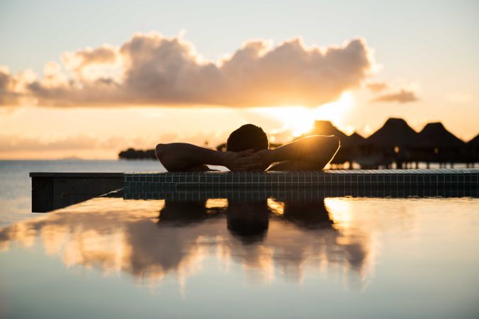 Silhouette of man sitting on bench near body of water during sunset