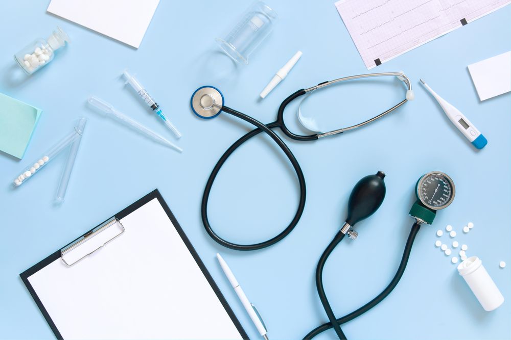 Top view of blue desk with scattered doctor’s equipment and notepad