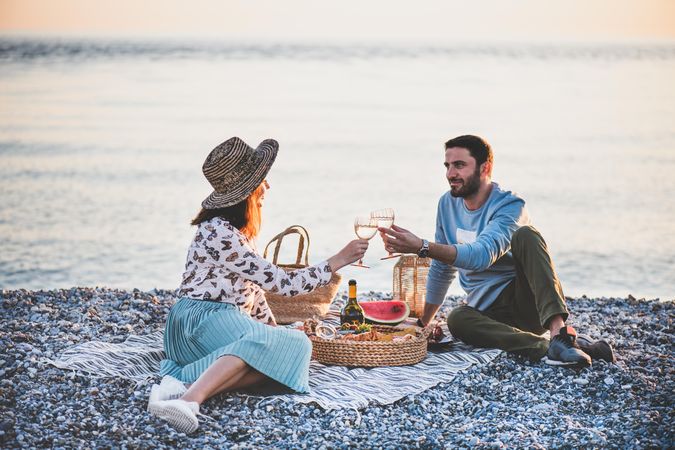 Couple toasting with wine glasses at summer picnic by the ocean