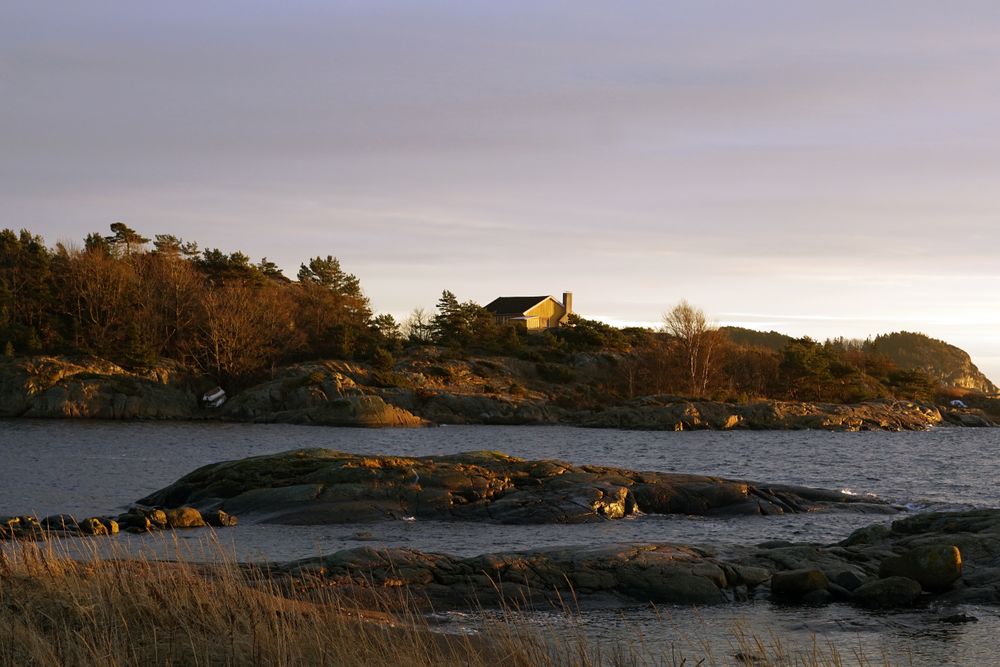 Rocky shore with house of tranquil sea in dusk