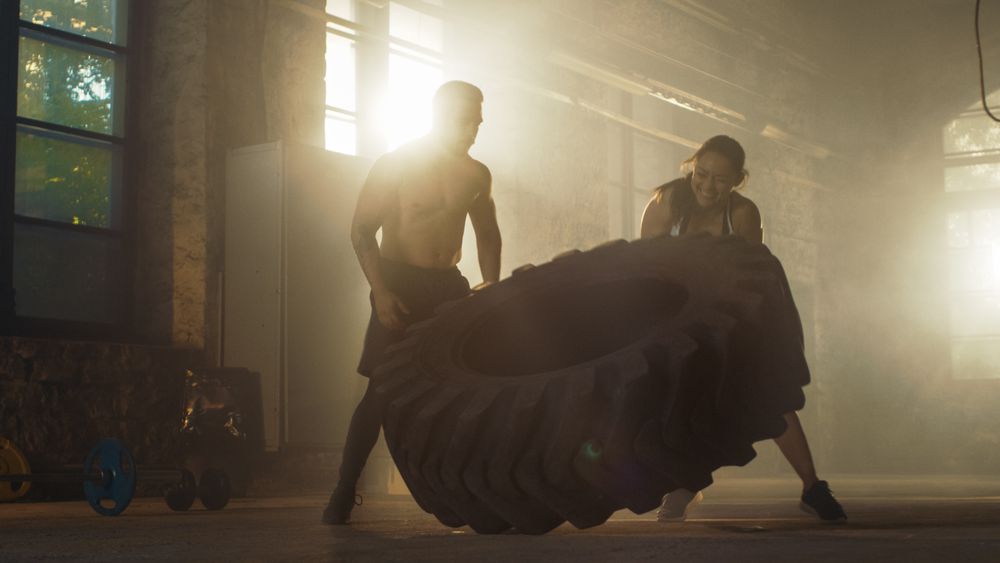 Fit Athletic Woman Lifts Tire Under Supervision of Her Partner  Trainer