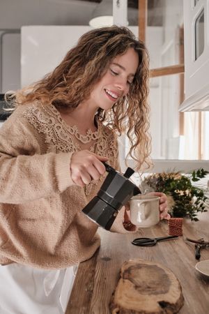 Smiling young woman pouring coffee in mug