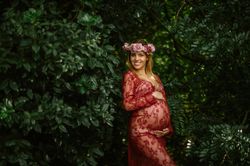 Pregnant woman with closed eyes touching belly and chin while standing in garden in sunny day