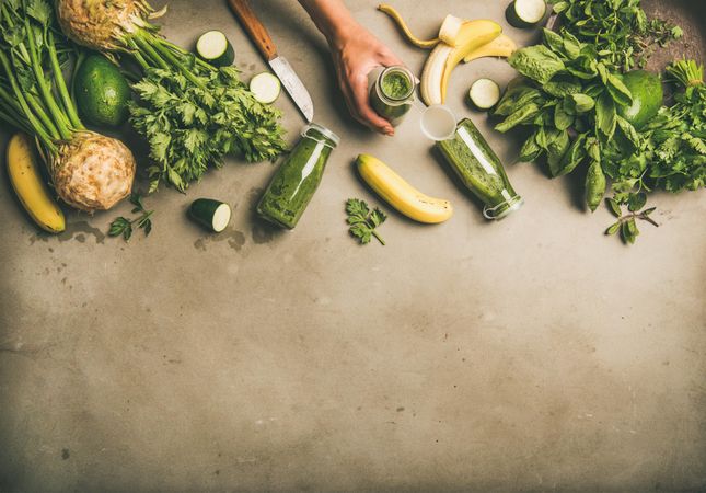 Smoothie ingredients with hands holding bottle, banana, zucchini, on grey table, with copy space