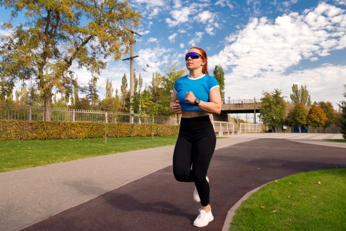 Woman jogs in park, wearing blue top and sunglasses
