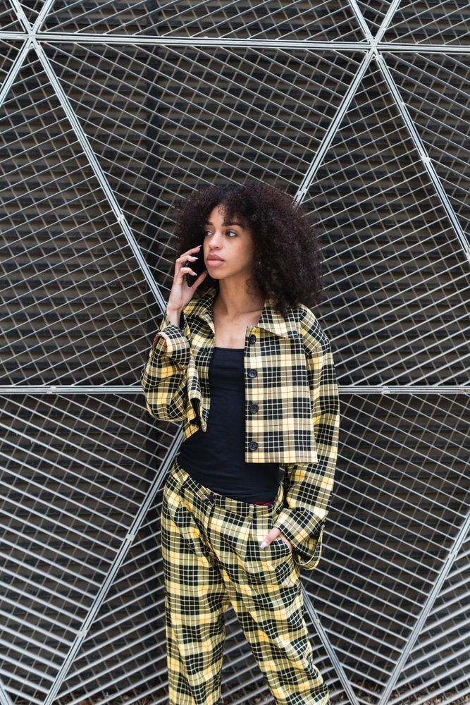 Trendy Black woman talking on smartphone against grid fence