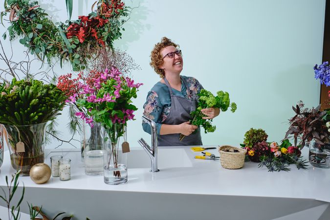 Woman arranging flower bouquet and laughing in floral shop
