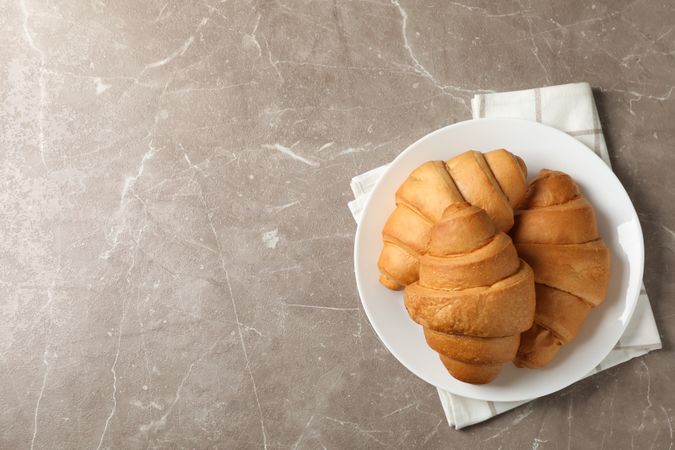 Plate with croissants on napkins on grey table, top view, copy space