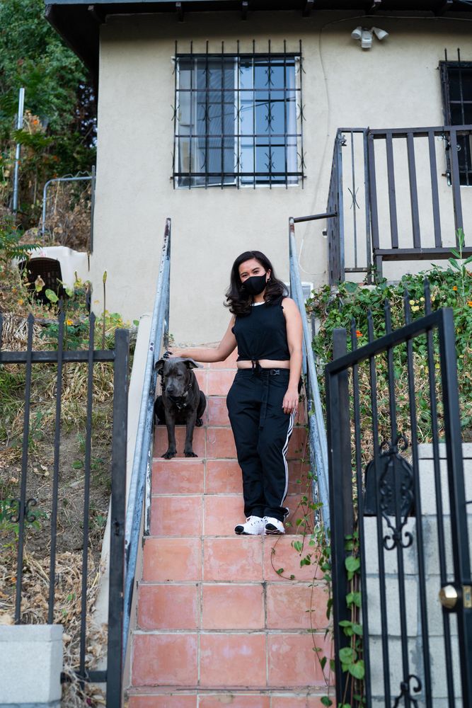 Woman in athletic gear and mask standing on her front steps in front of her house