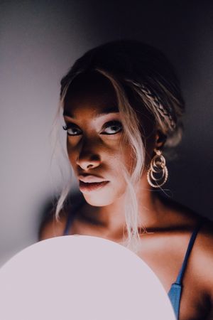 Black adult woman with illuminated balloon in darkness looking at camera