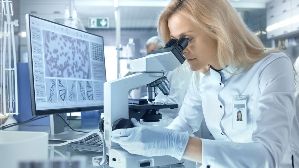 Female Research Scientist Looks at Biological Samples Under Microscope.