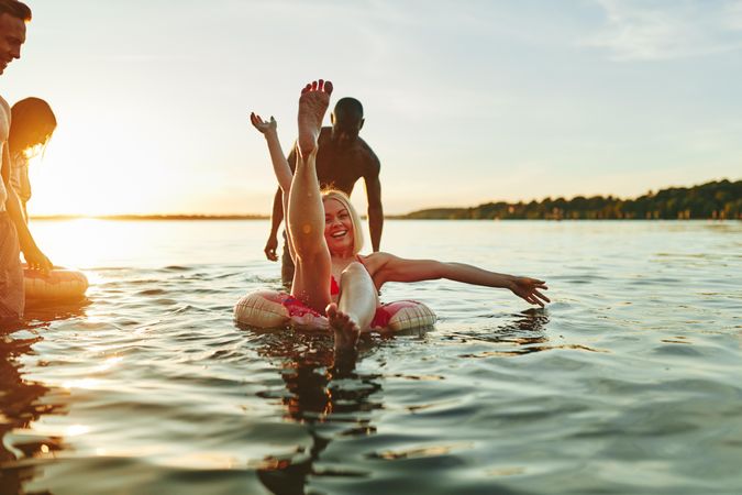 Woman with her leg up while floating in a ring on a lake with her friends