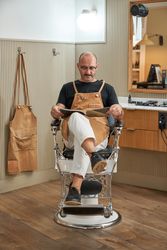 Confident barber sitting with magazine in barbershop