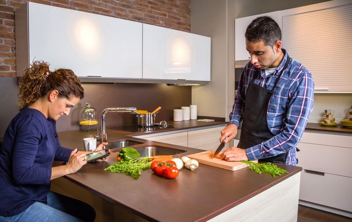 Woman checking digital tablet as her and her partner prepares meal