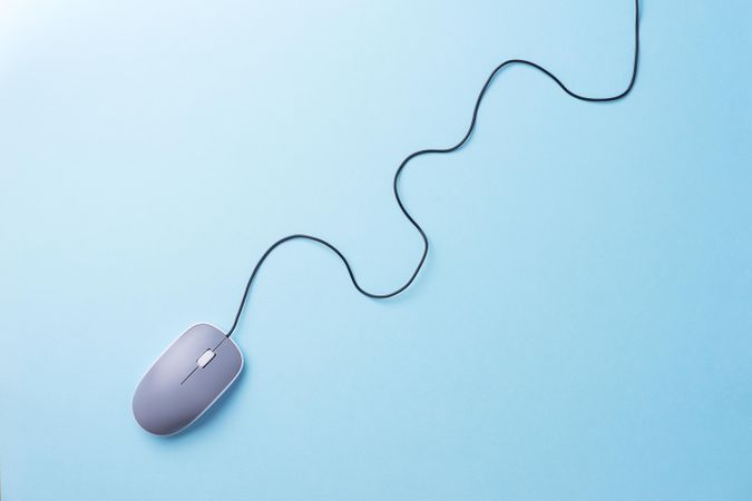 Computer mouse with cable attached laying diagonally on light blue background in