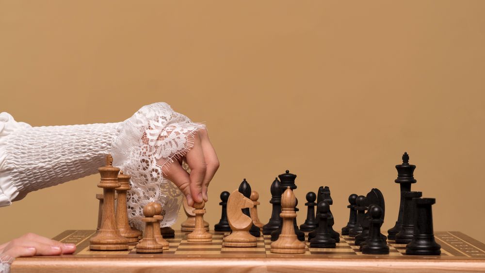 Hand in lace sleeve adjusting chess piece during game.
